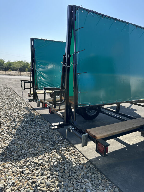 Two green banner trailers on gravel.