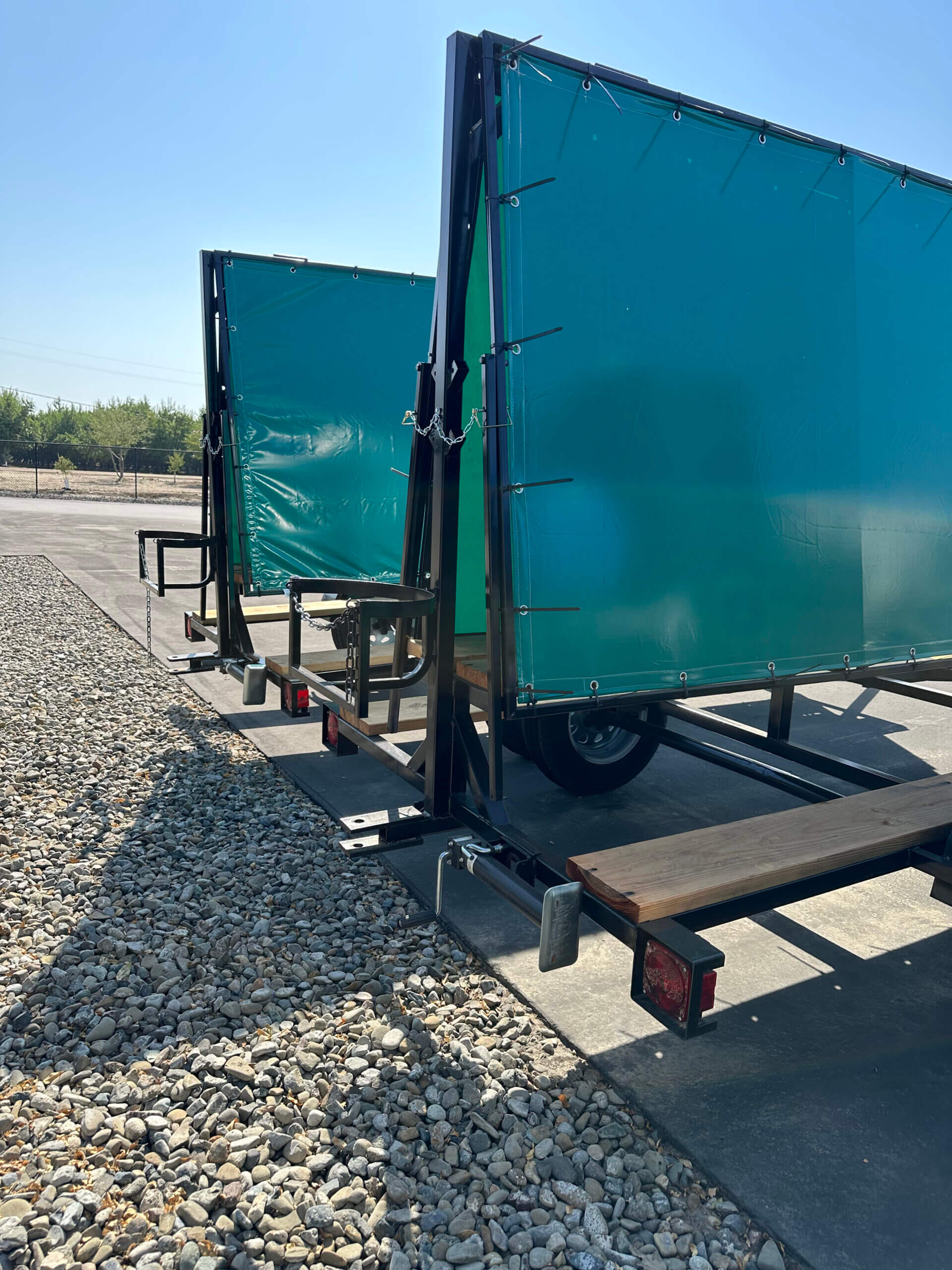 Two green banner trailers on gravel.