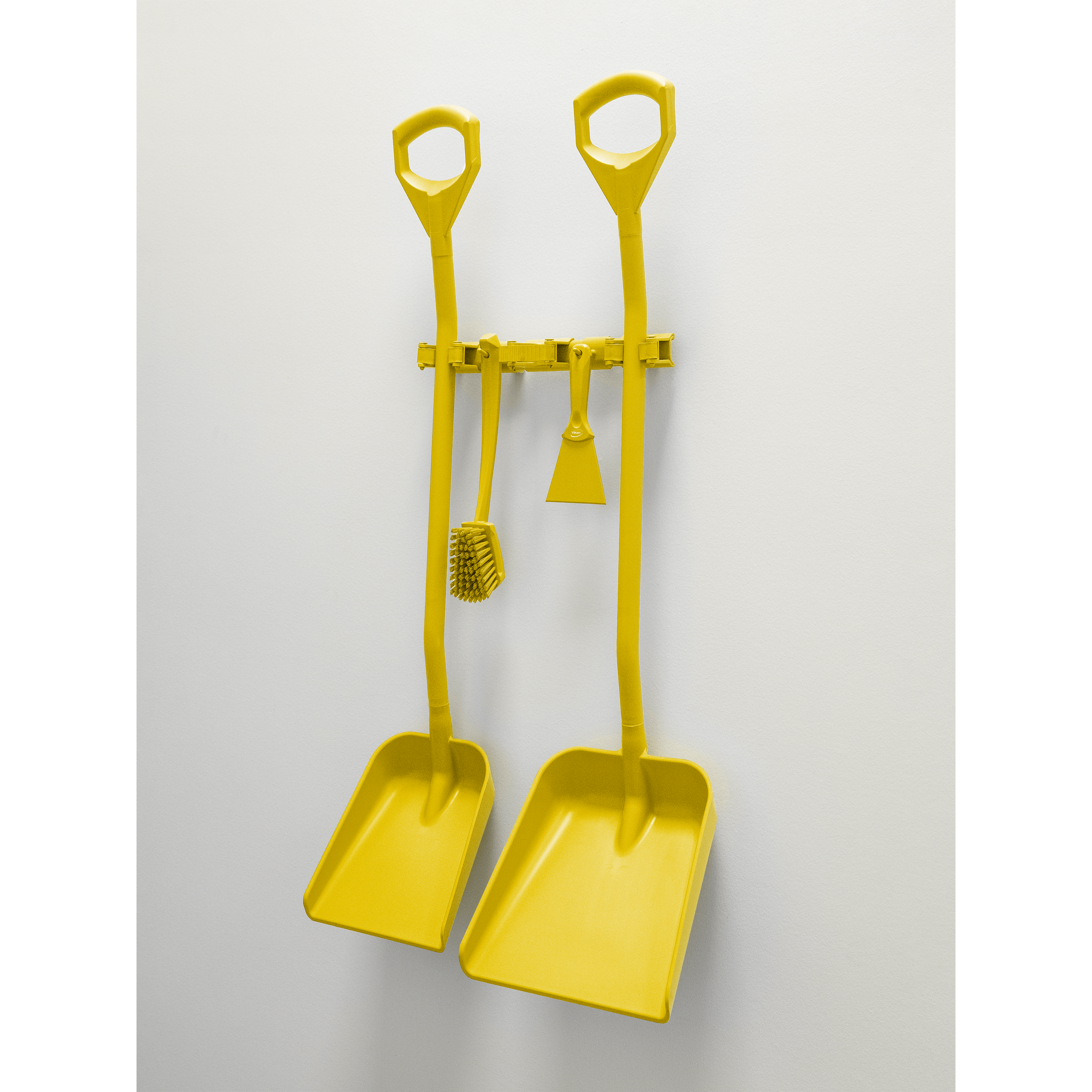 Two yellow dustpans and a brush on a wall.