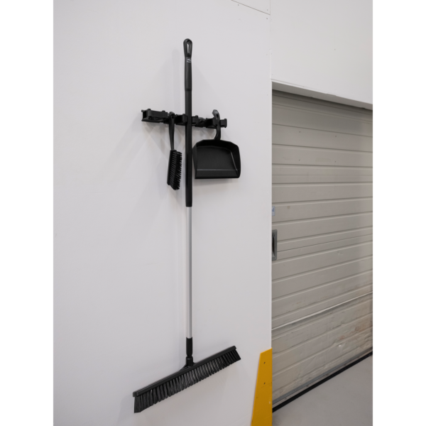 Black broom and dustpan hanging on wall.