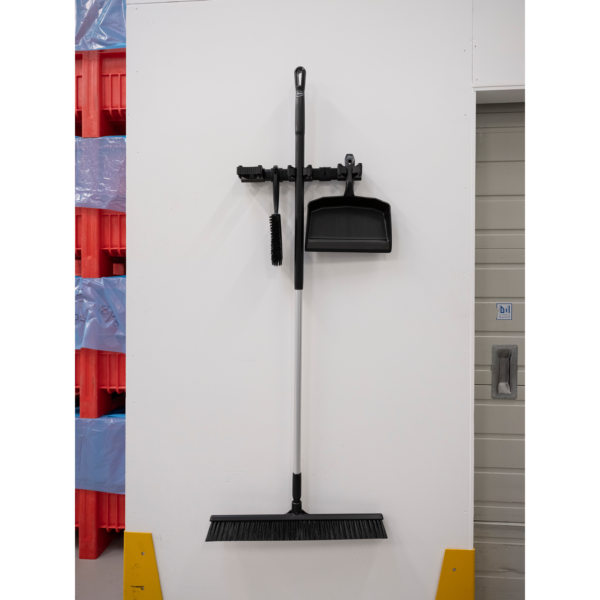 Black broom and dustpan hanging on wall.