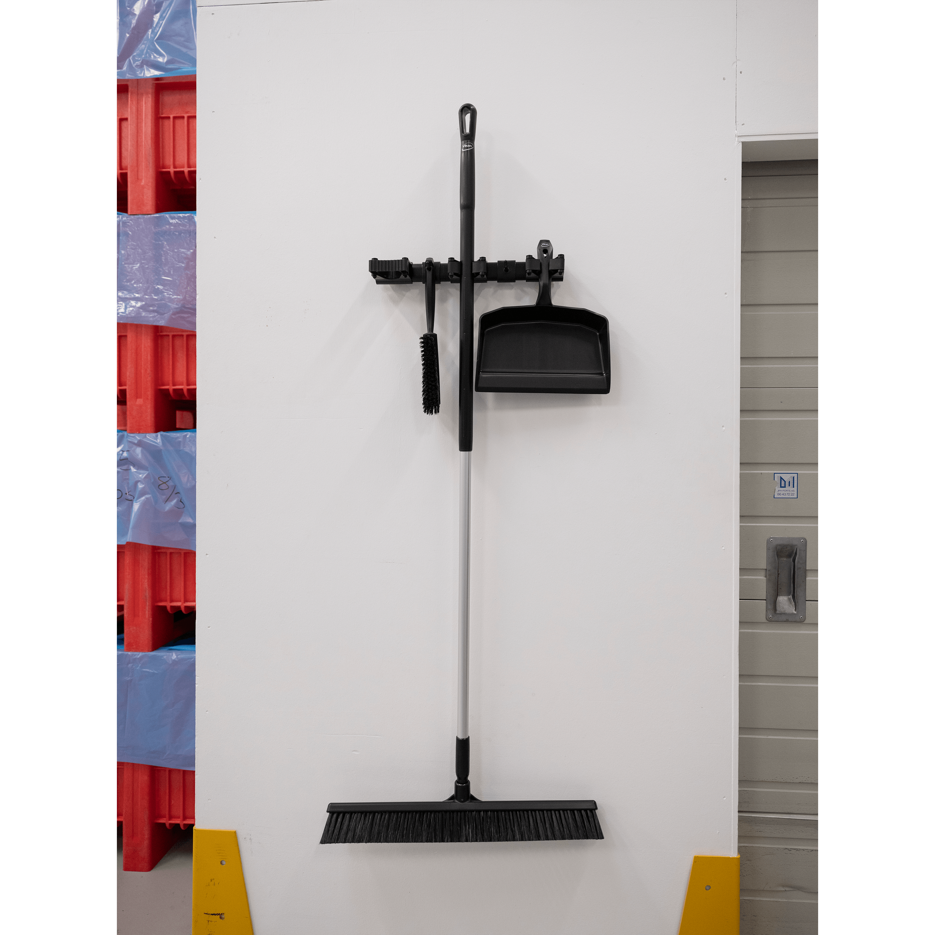 10119-3 Black broom and dustpan hanging on wall.