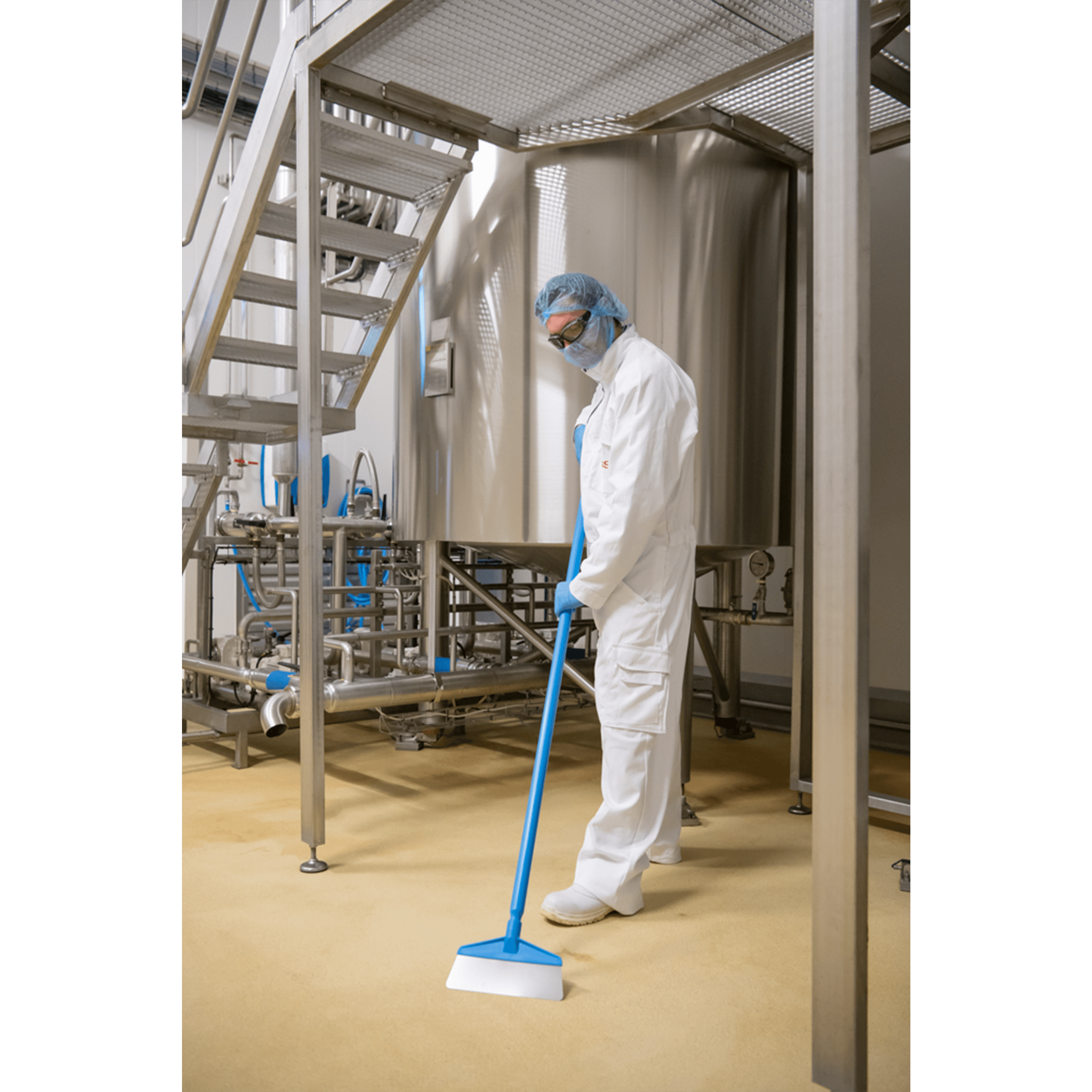 Worker cleaning factory floor with a squeegee.