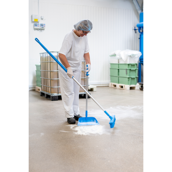 Worker sweeping floor in industrial setting.