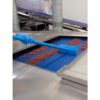 Blue tool cleaning red granules on conveyor belt.