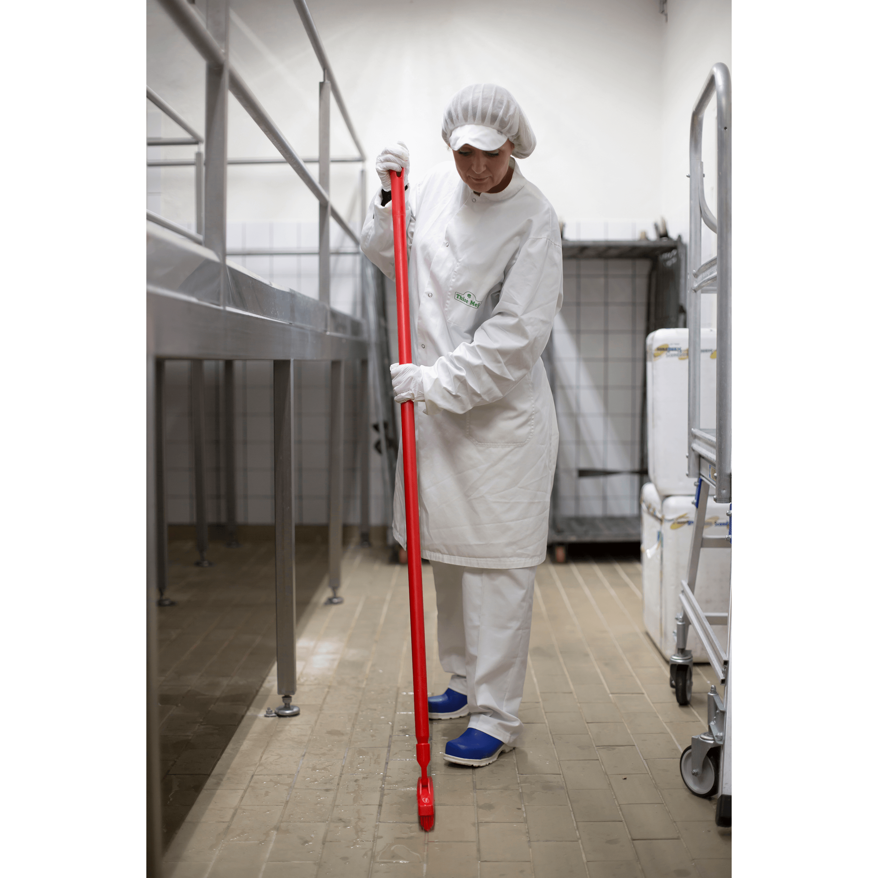 29607-4 Woman in white scrubs cleans tiled floor.