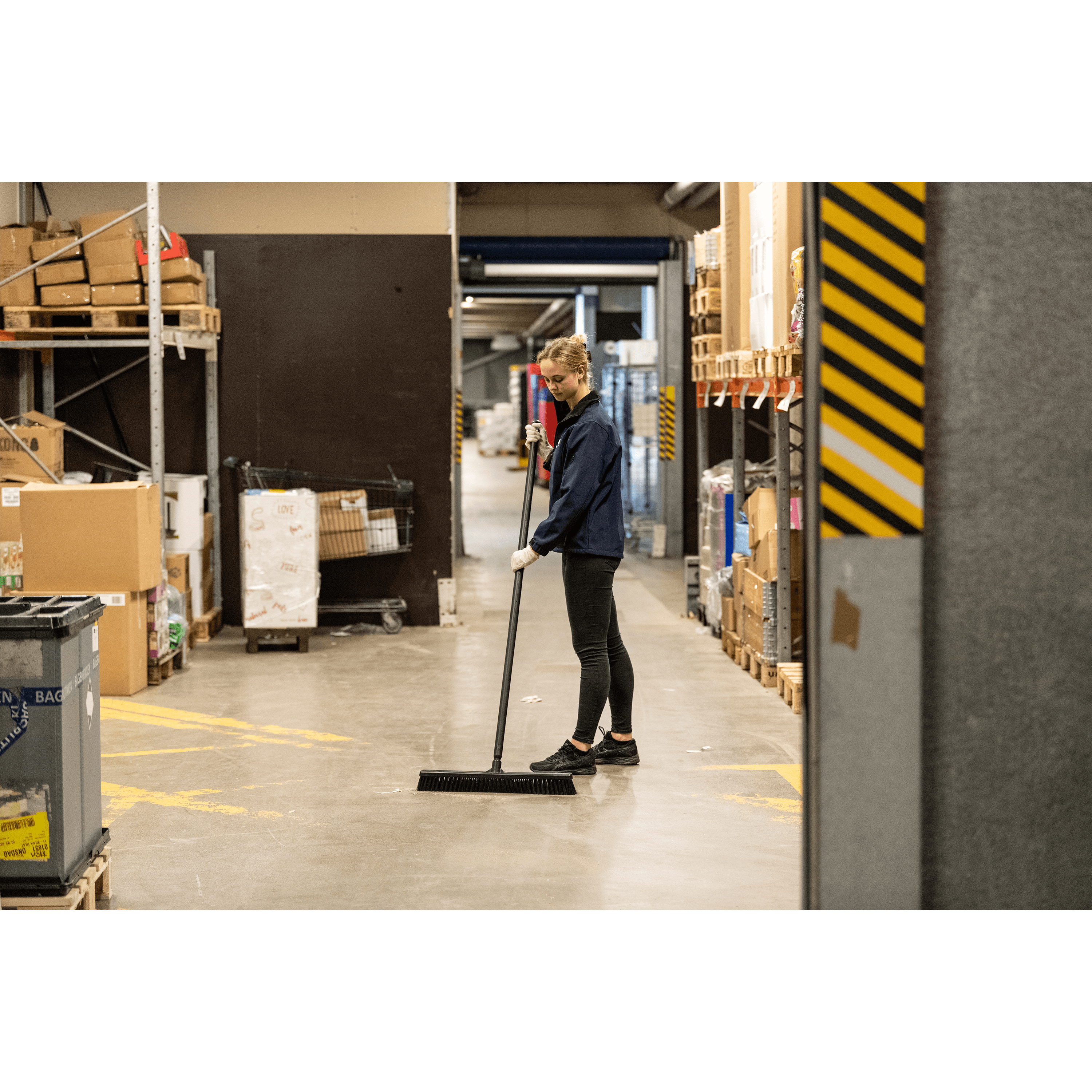 29626-4 Woman sweeping warehouse floor with broom.
