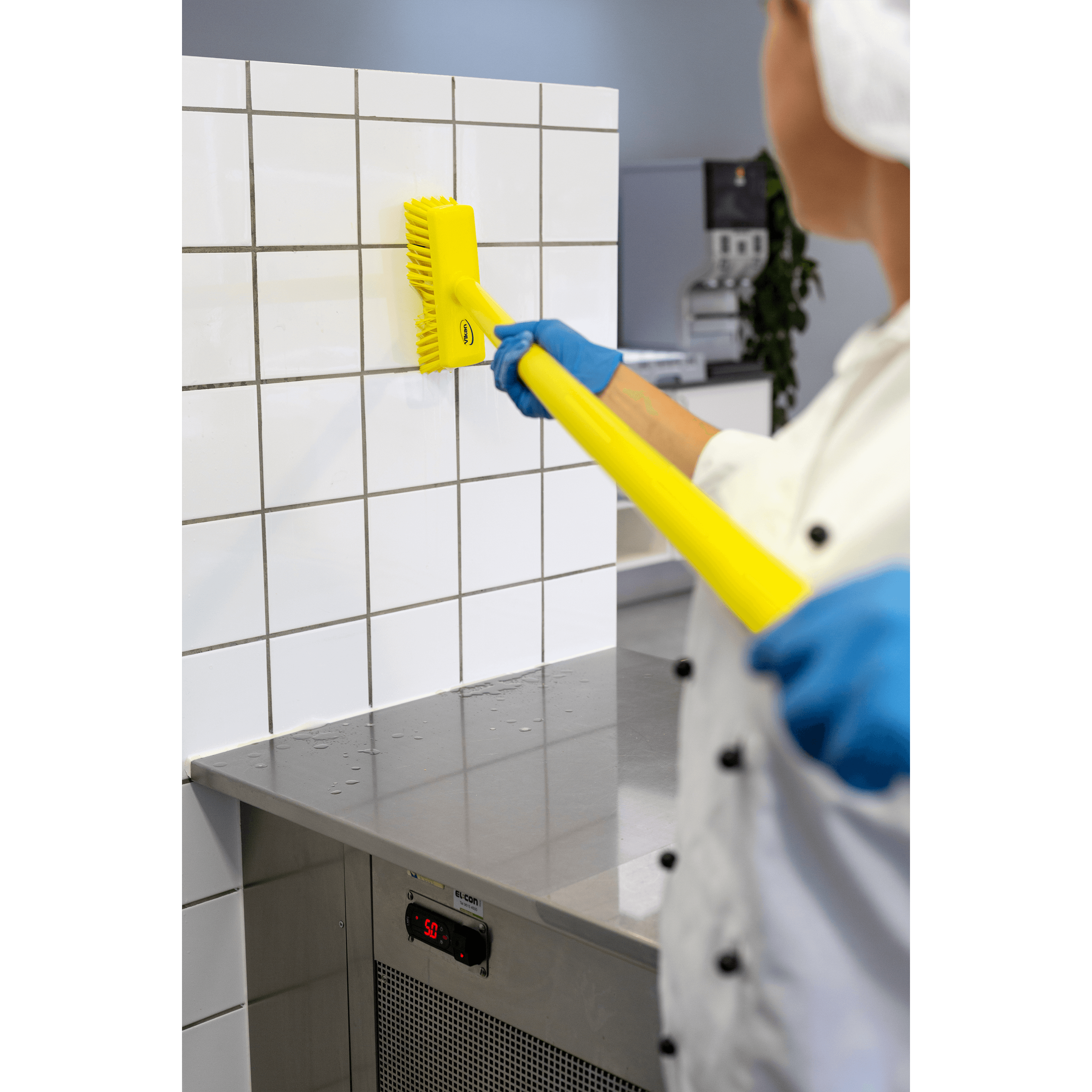 29626-5 A person cleaning white tile with a yellow brush.