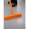 Orange broom sweeping up debris on floor.