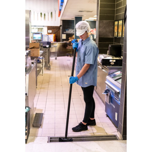 A person cleaning a floor drain with a brush.