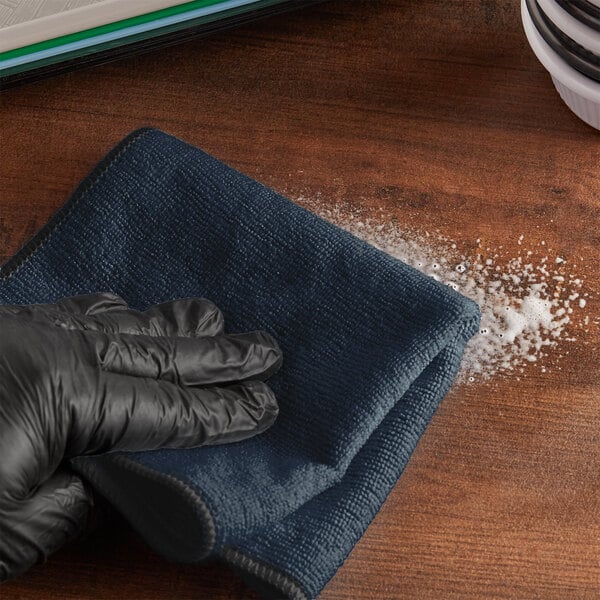 A gloved hand wiping a wooden surface.