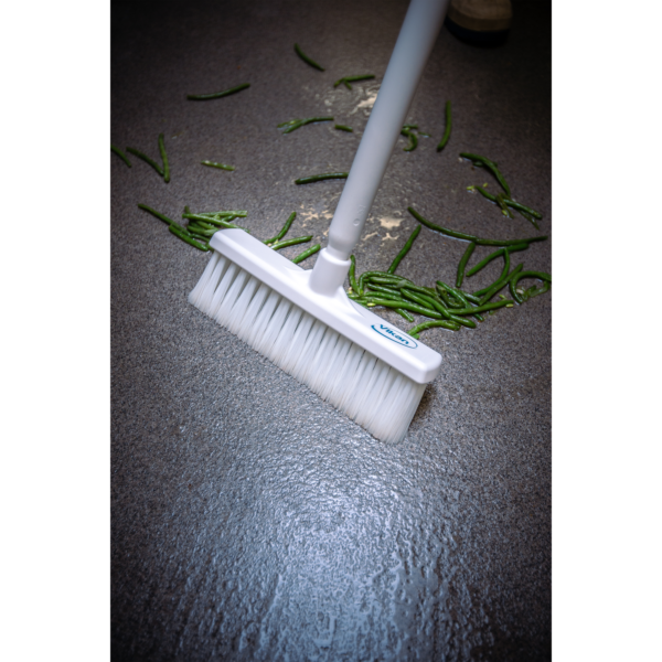 White broom sweeping green beans on floor.