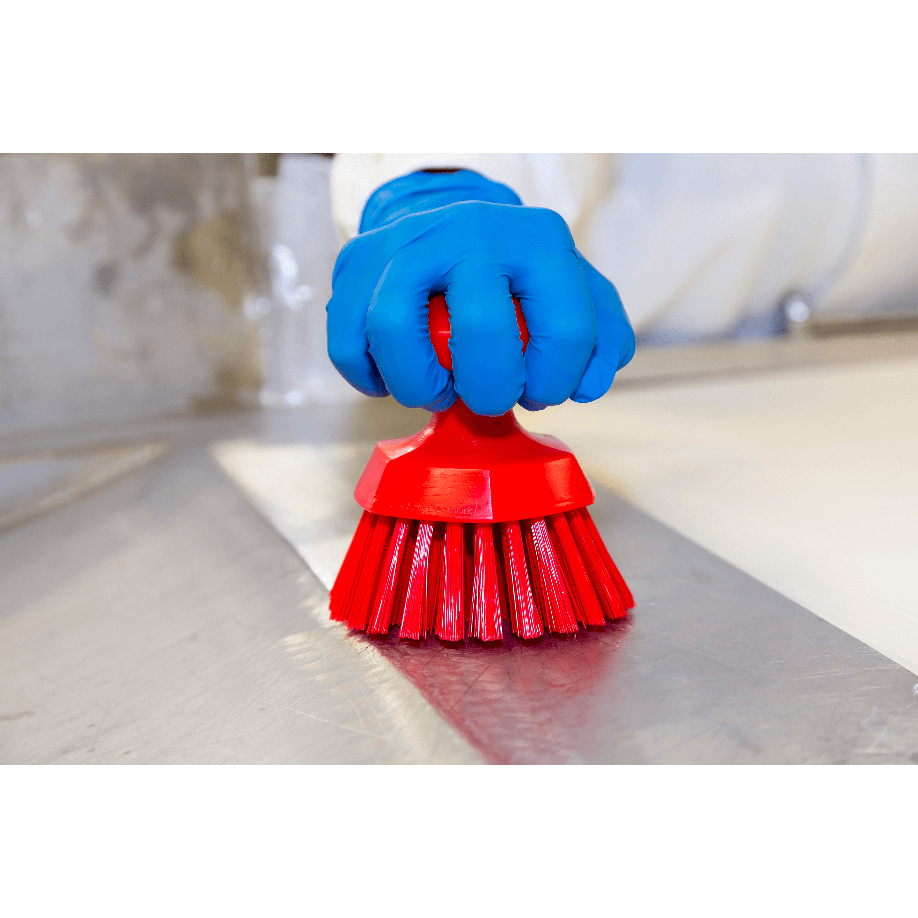 A gloved hand holding a red brush.