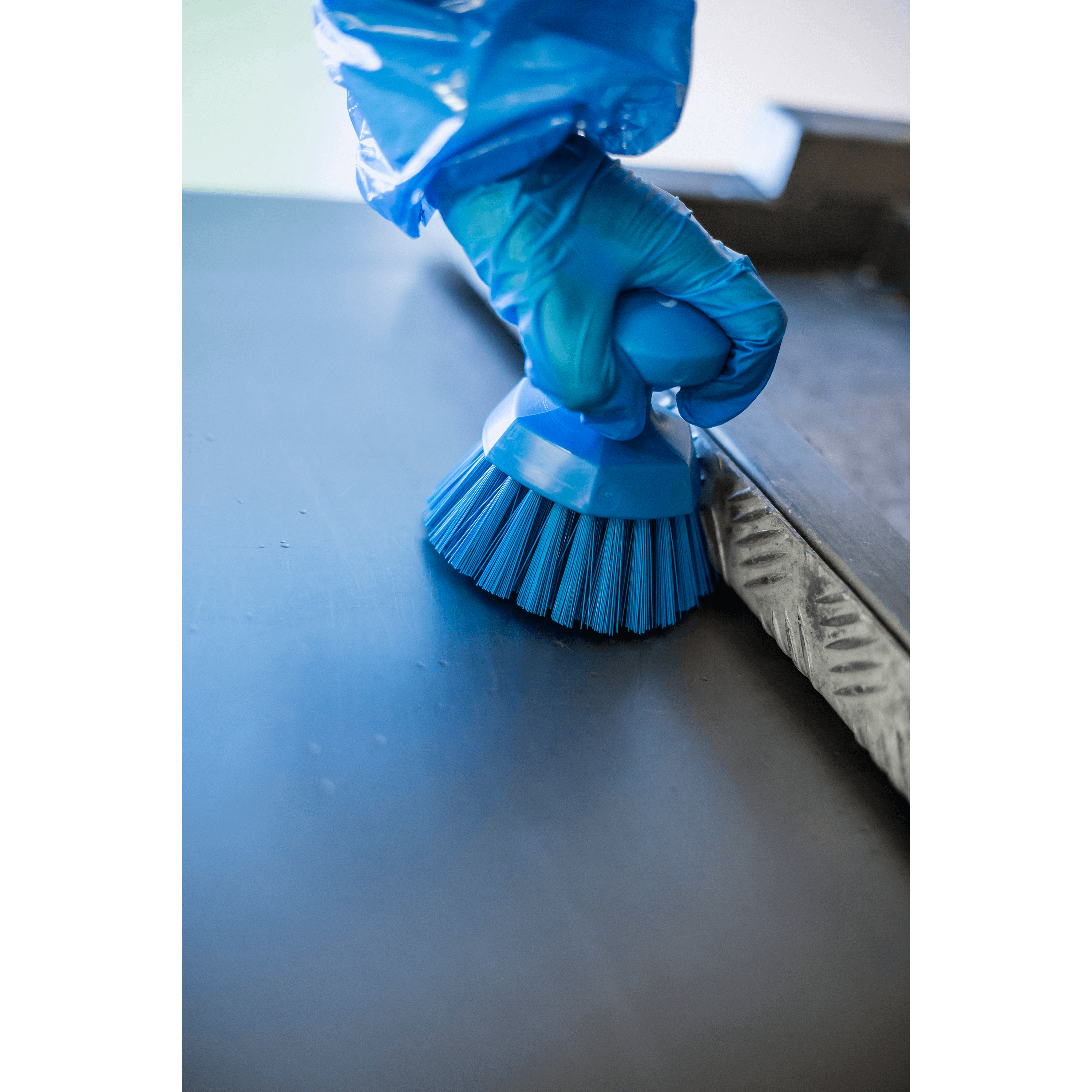 A gloved hand scrubs a surface with a blue brush.