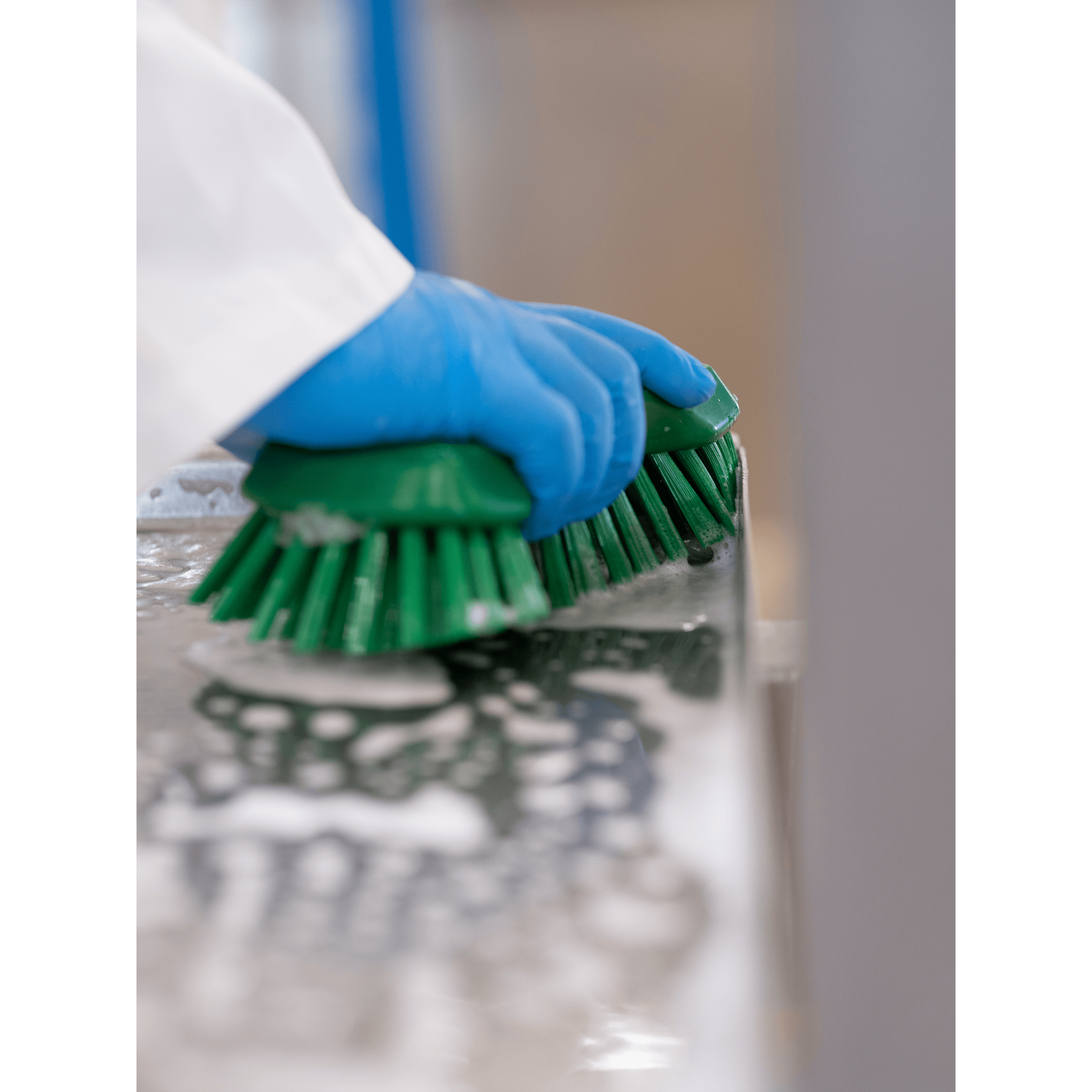 Hands scrubbing a surface with green brushes.