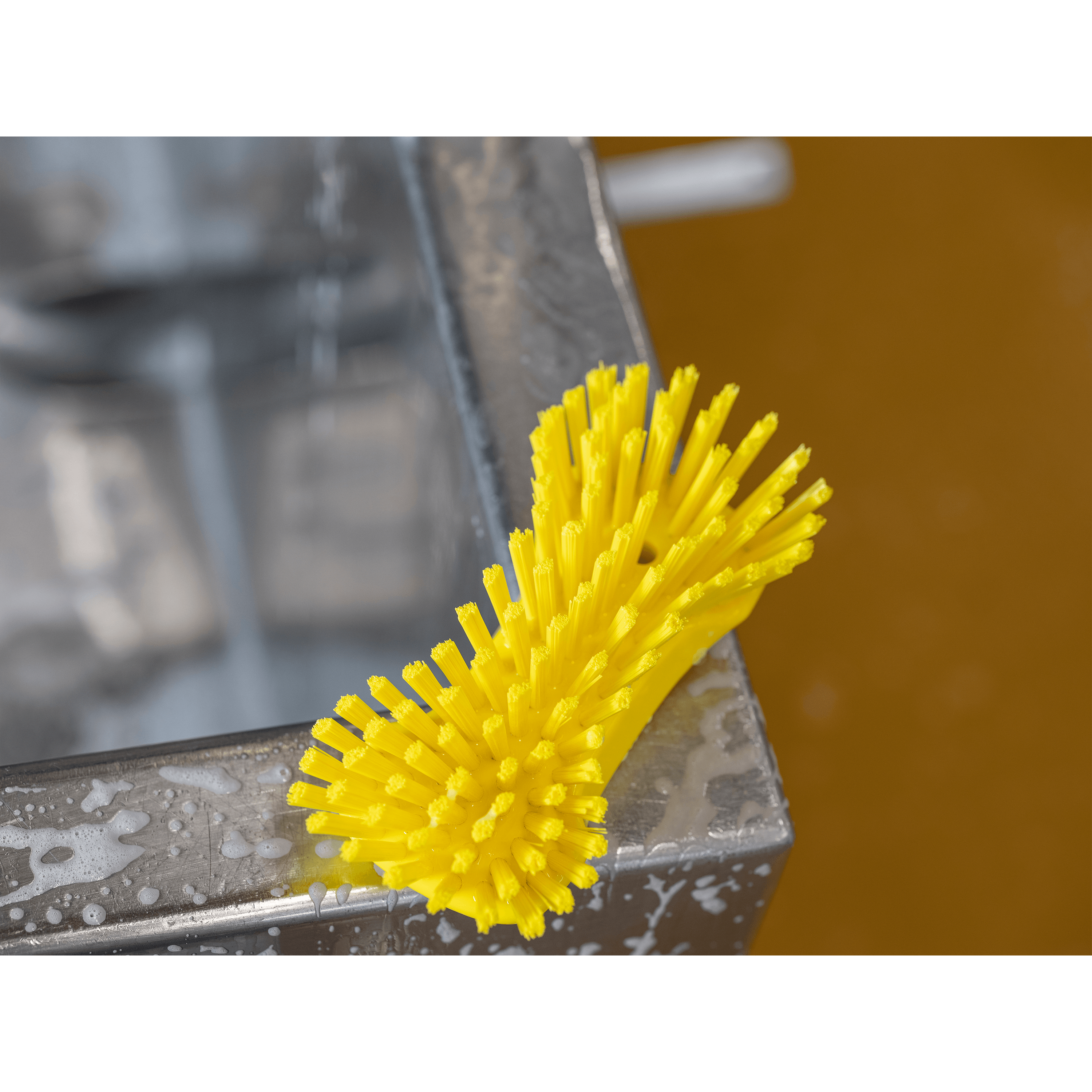 Yellow cleaning brush on a metal surface.