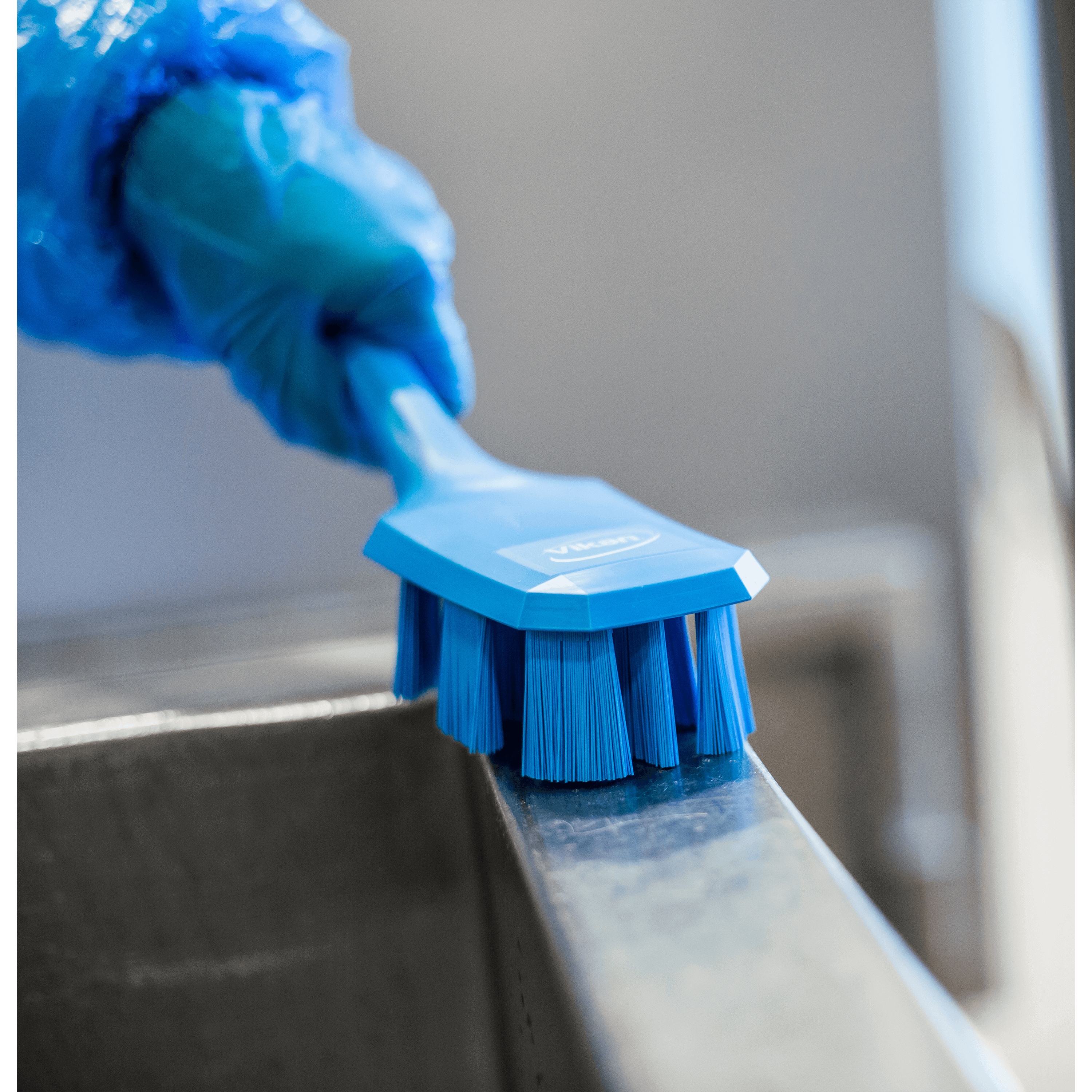 Blue cleaning brush in gloved hand.