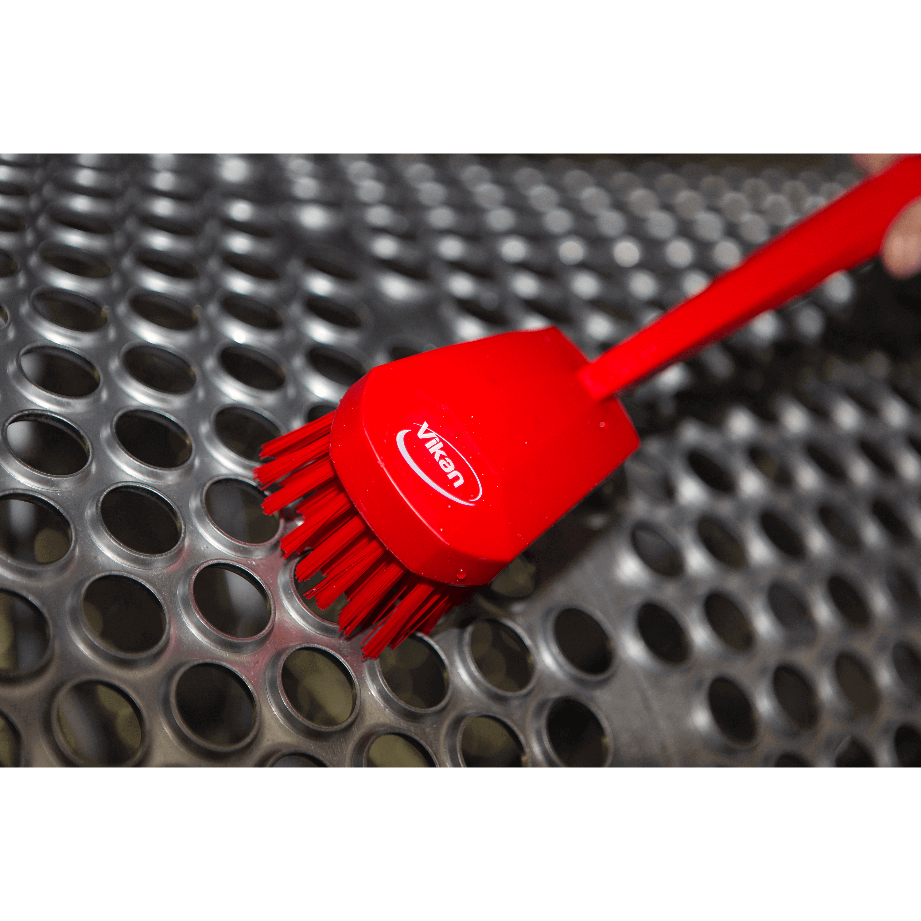 Red brush cleaning a perforated surface.