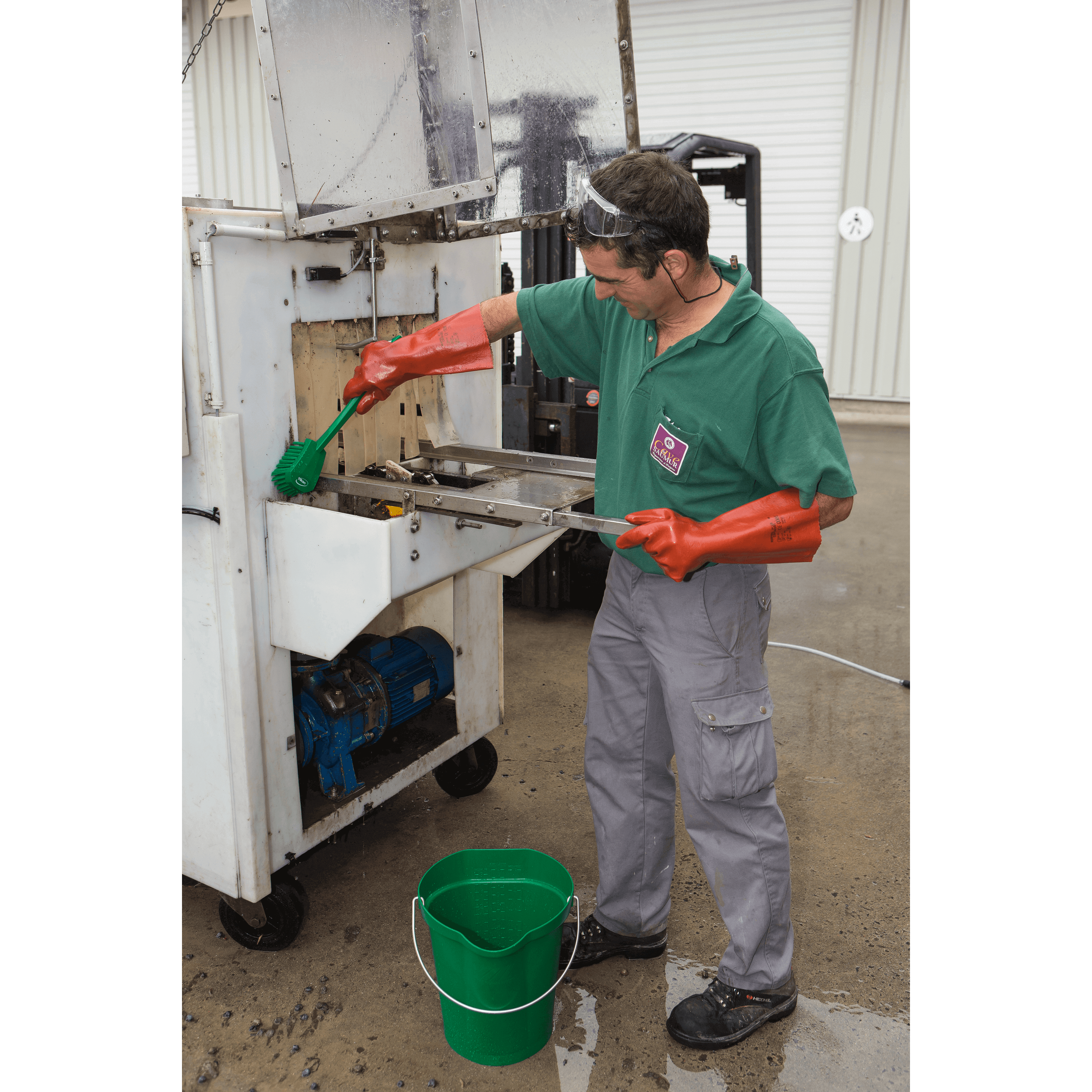 Man cleaning equipment with green brush.