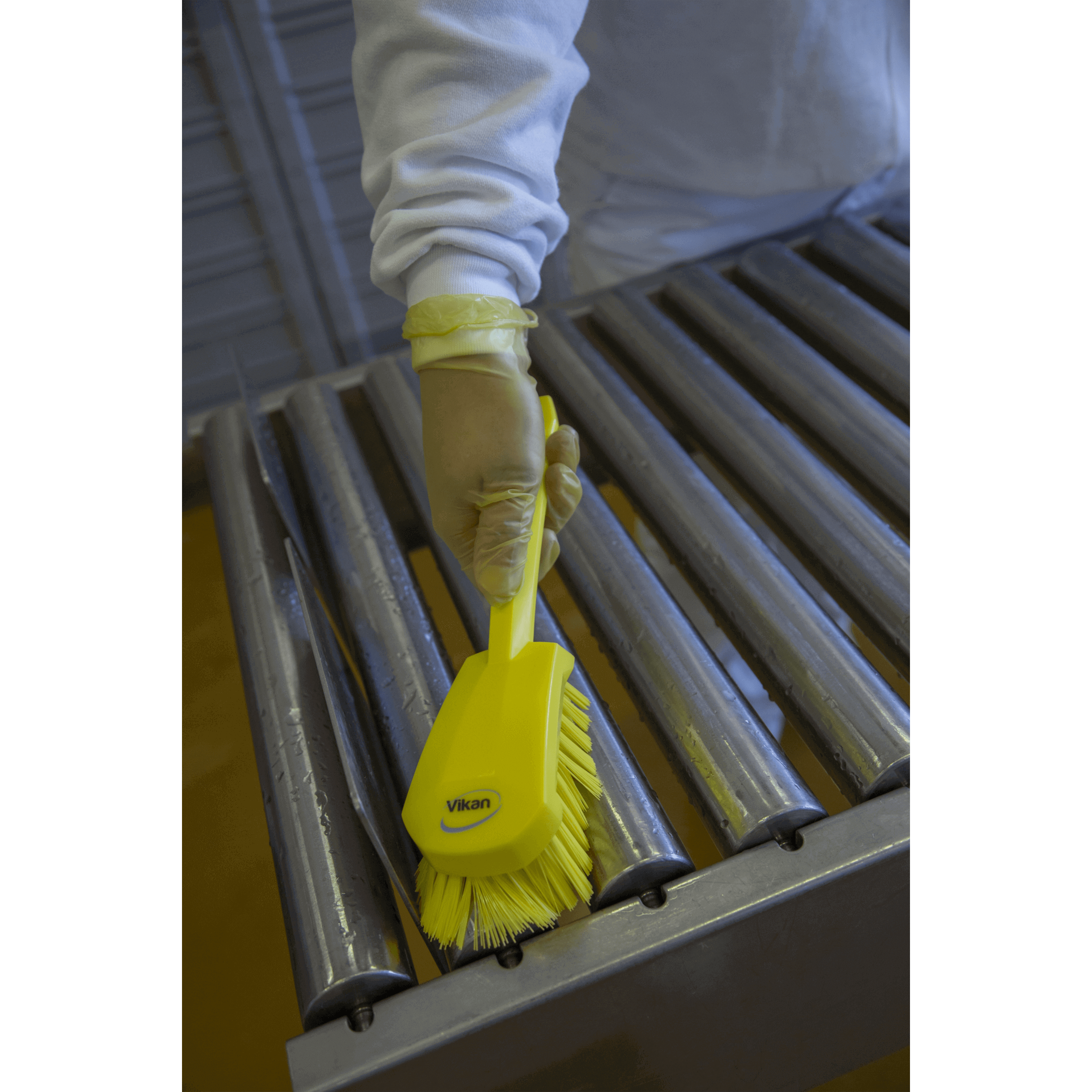 Person cleaning conveyor with yellow brush.